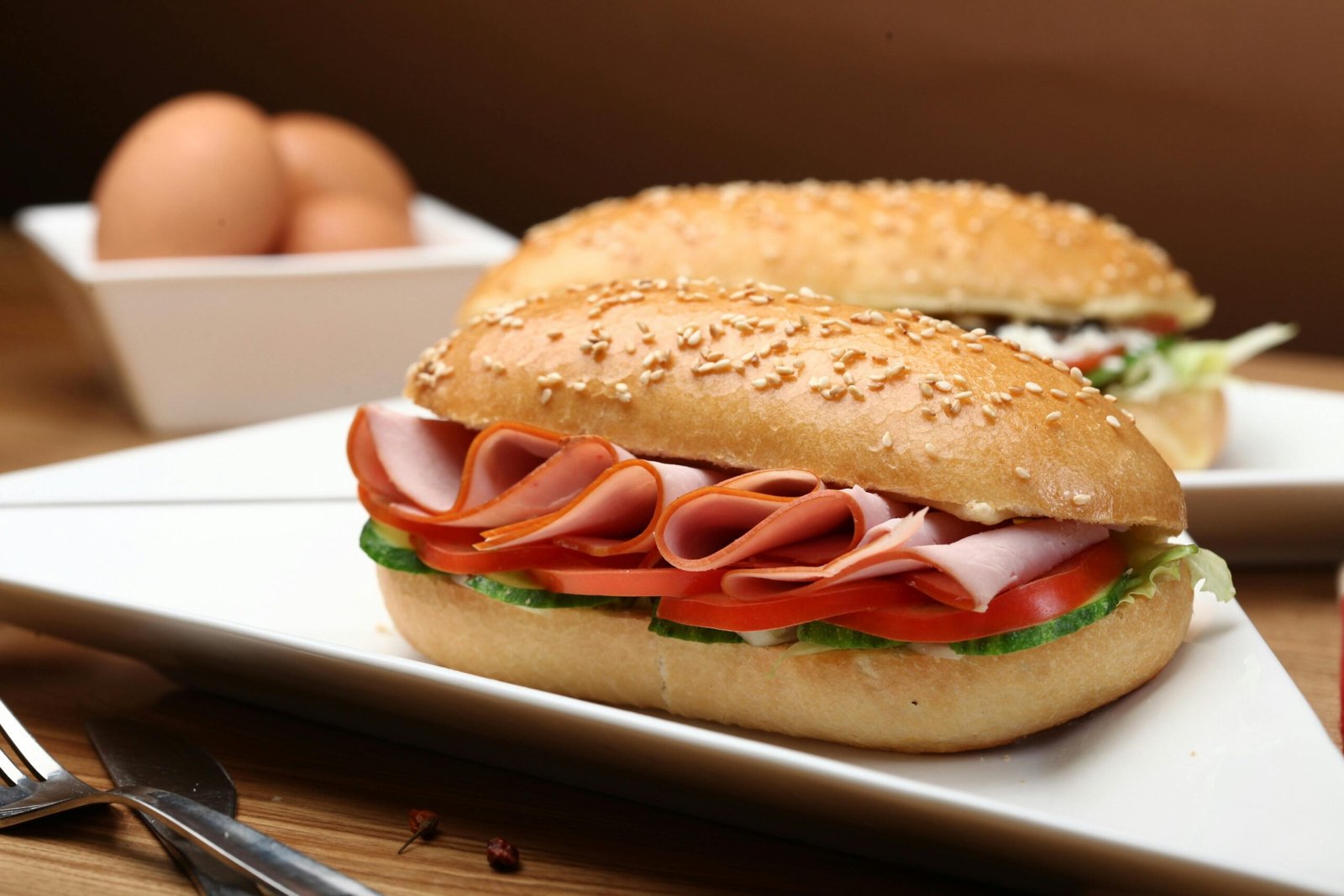 Tasty ham and vegetable sandwich on sesame bun with fresh ingredients served on a white plate.