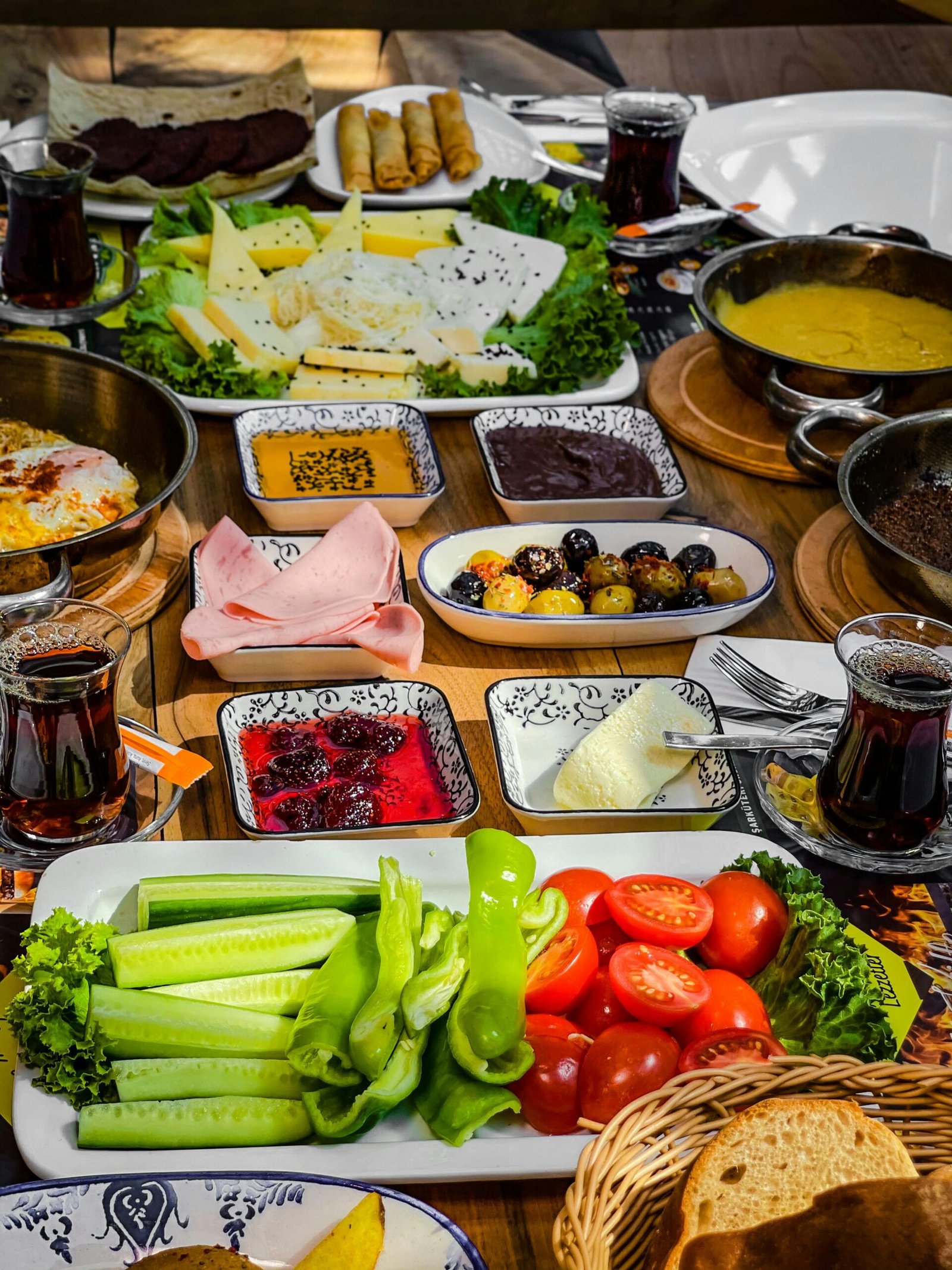 Vibrant Turkish breakfast spread with fresh vegetables, cheeses, jams, and hot tea served on a rustic wooden table.